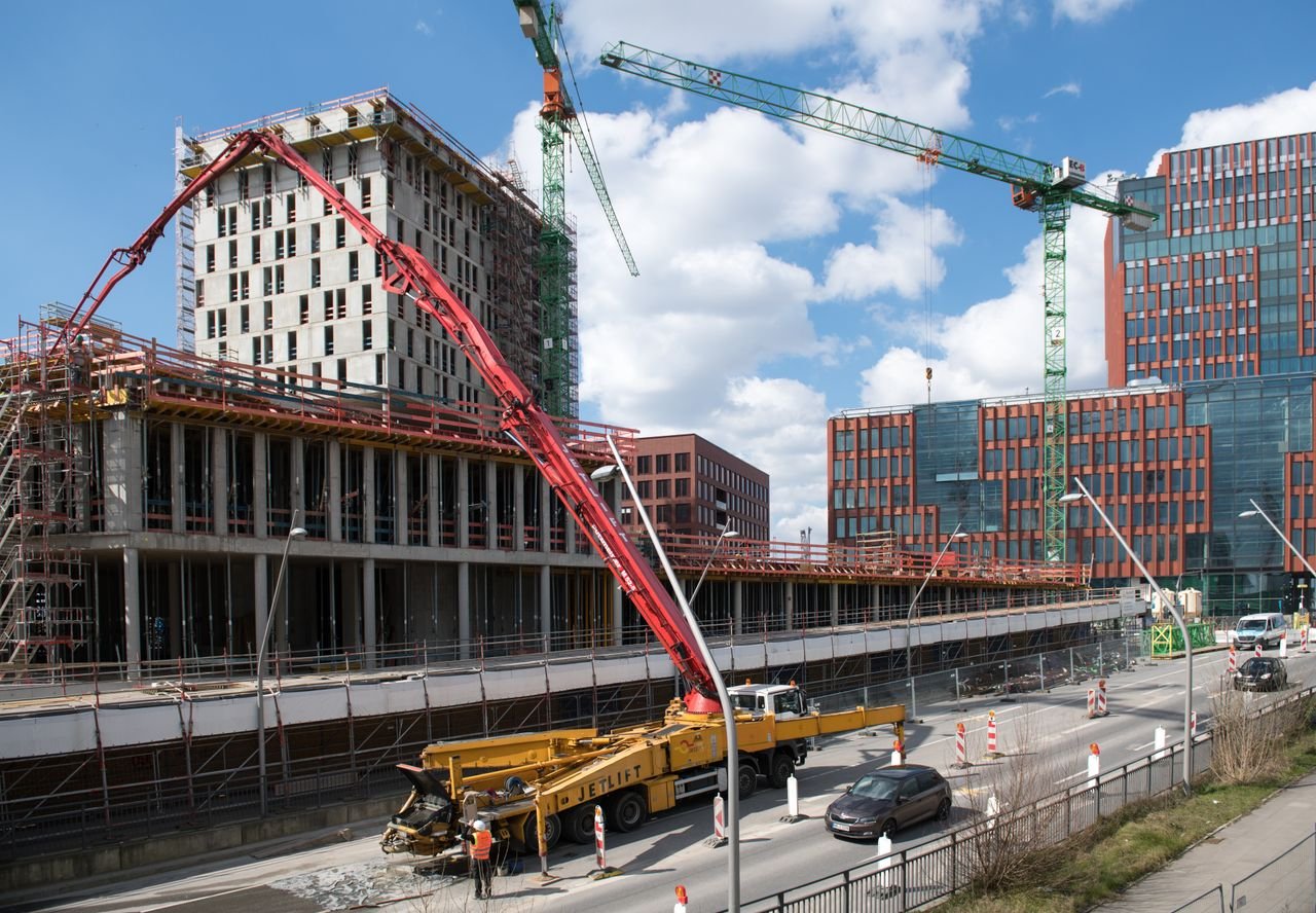 Artisans et métiers du bâtiment à Paris et en Île-de-France Busy construction site in Hamburg with cranes and trucks under a clear sky. – Couvreur dans les Yvelines (78)