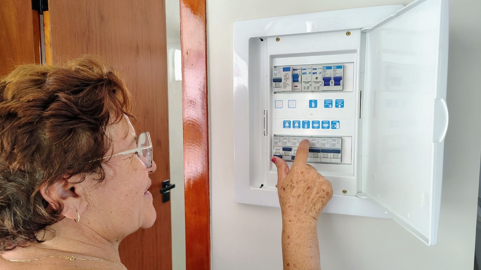 Électricité à Paris et en Île-de-France Femme senior ajustant une boîte à fusibles électrique – Électricité Maison en Essonne (91)